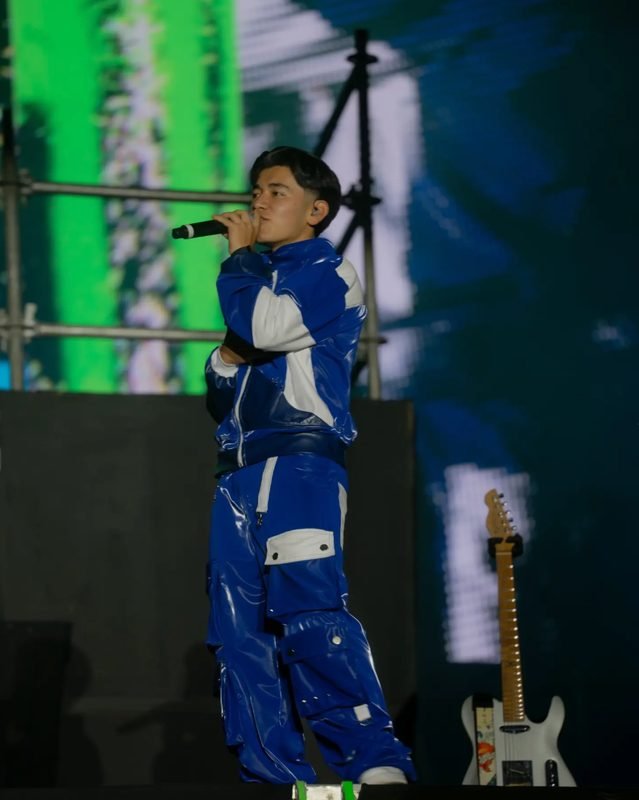 Un integrante de Picus canta al micrófono con un conjunto azul y blanco