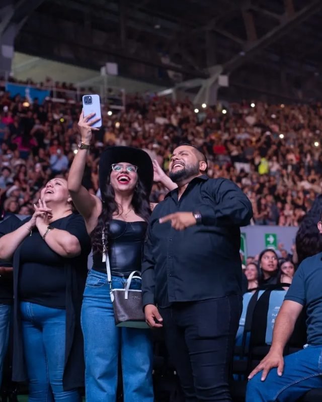 Asistentes de pie cantan y graban con el celular; al fondo, las gradas llenas