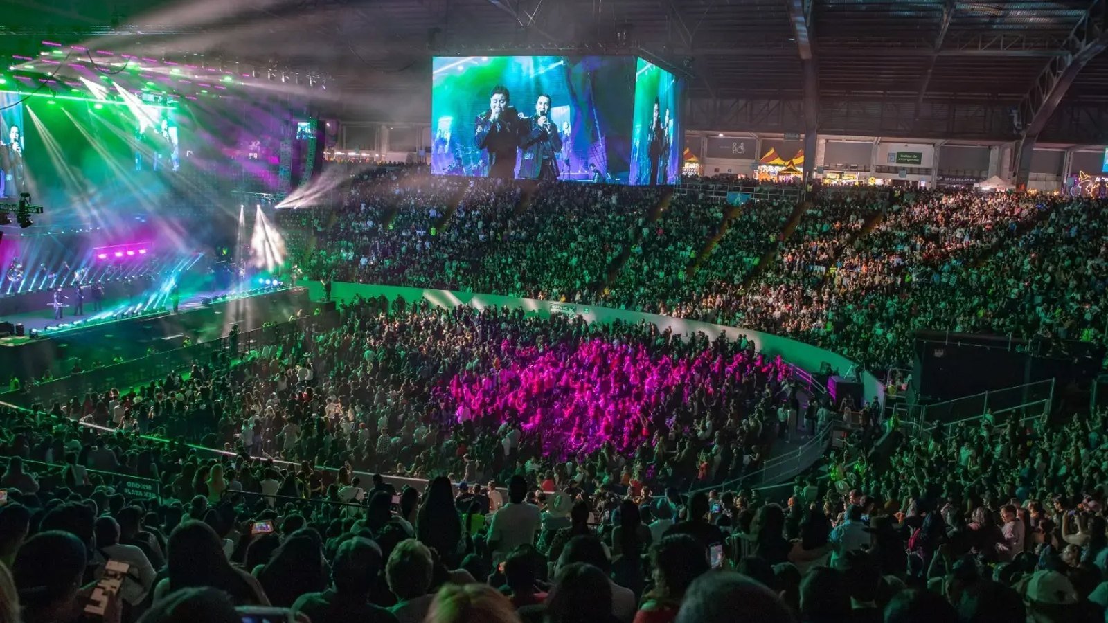 Vista panorámica del Auditorio Jalisco lleno durante el concierto de La Arrolladora: pista y gradas repletas, luces verdes y las pantallas gigantes mostrando a los vocalistas