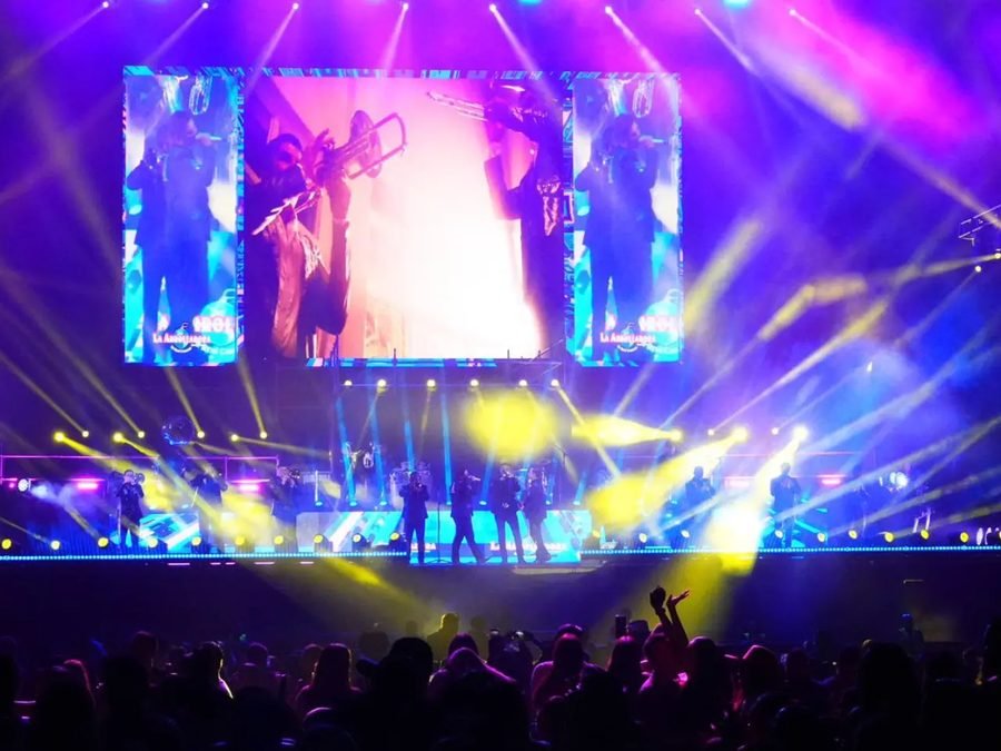El escenario bañado en luces moradas y amarillas; las pantallas muestran a un trompetista de la banda