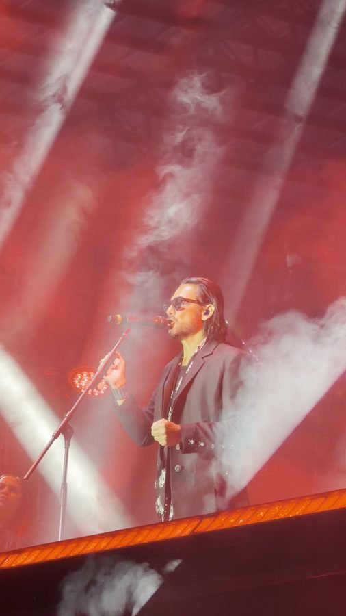 Beto Cuevas canta entre haces de luz rojos y humo, con saco negro y lentes oscuros