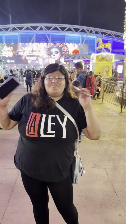 Una fan con playera de La Ley sostiene su boleto frente a la rueda de la fortuna