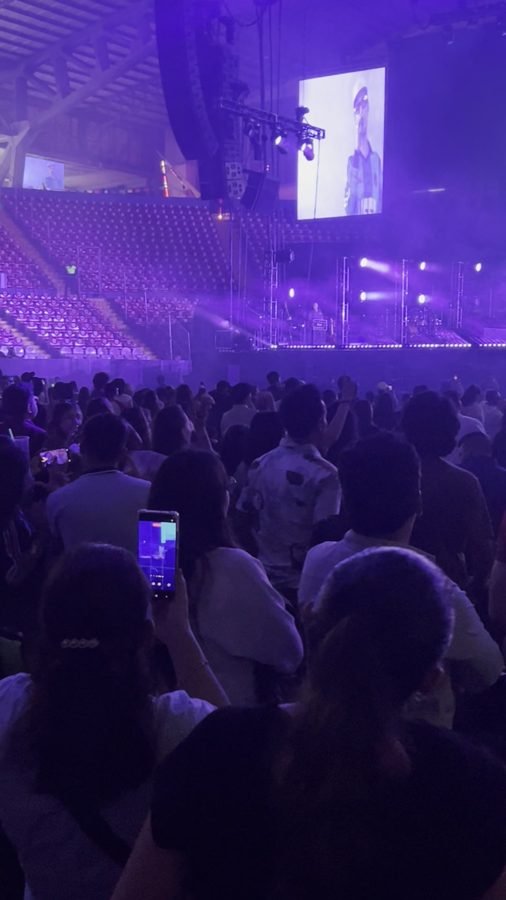 El Foro Principal en luz morada, con el público de pie frente al escenario y las pantallas laterales encendidas