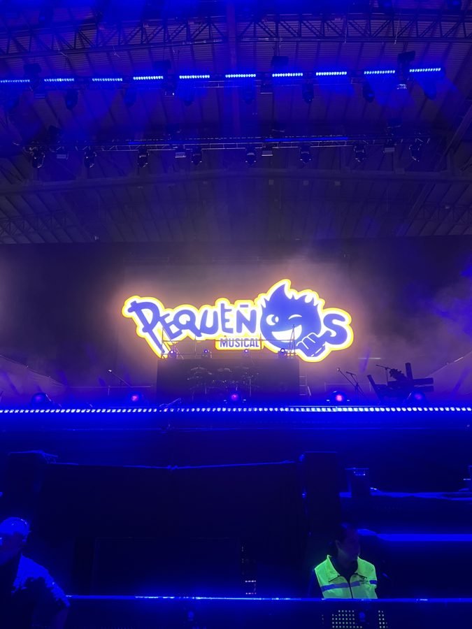 La pantalla del escenario muestra el logo de Pequeños Musical en azul antes del concierto