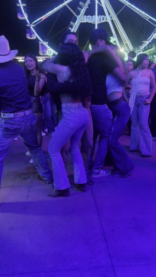 Parejas bailando en el pasillo de la feria de noche con la rueda de la fortuna al fondo