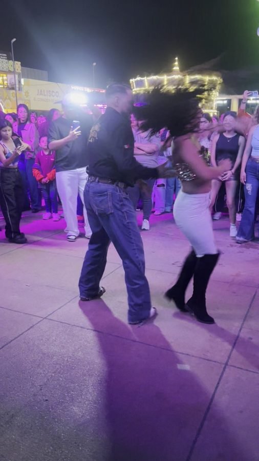 Una pareja baila abrazada en un pasillo de las Fiestas de Octubre con gente alrededor