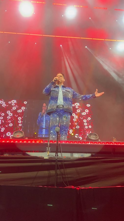 Vocalista de Pequeños Musical con traje de lentejuelas azules canta frente a una pantalla llena de margaritas, bajo luz roja