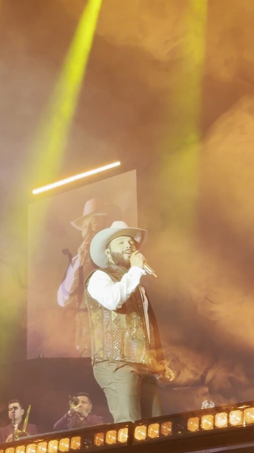 Leonardo Aguilar canta bajo luces doradas y humo, con su imagen en la pantalla