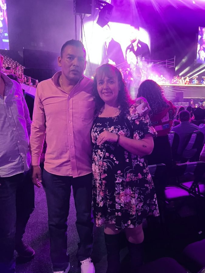 Una pareja posa abrazada en la pista con el escenario iluminado detrás