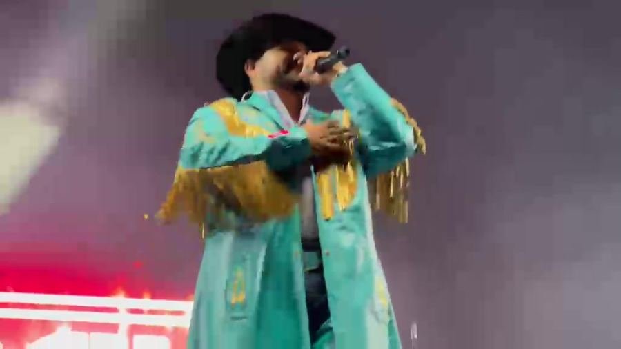 Un vocalista de Banda Machos con gabardina turquesa de fleco dorado y sombrero negro