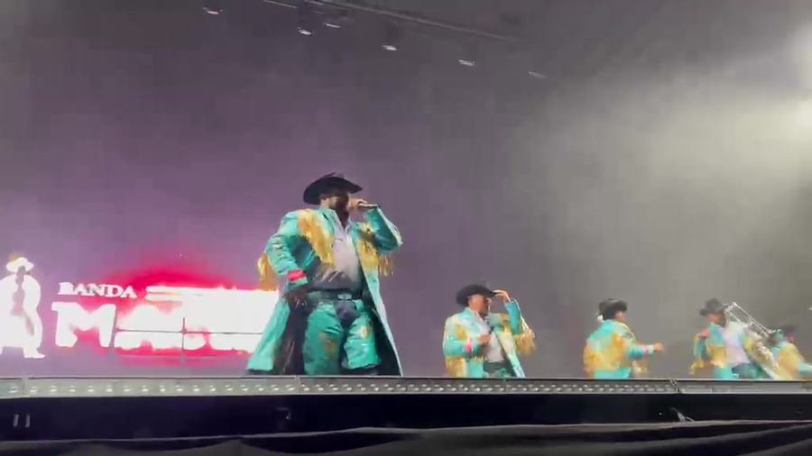 Banda Machos en el escenario con gabardinas turquesa y su nombre en la pantalla