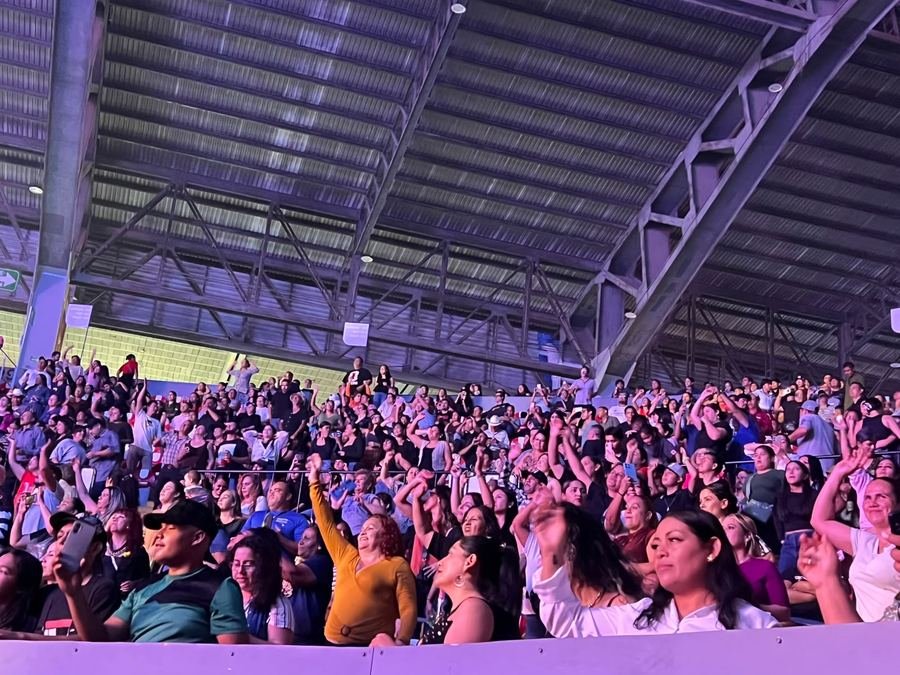 Gradas llenas de gente bailando con los brazos en alto bajo el techo del Auditorio