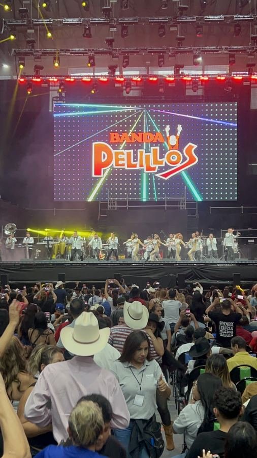 Banda Pelillos con sacos plateados y bailarinas frente a su logo en la pantalla