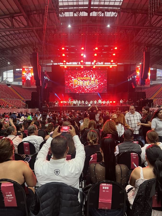 Un asistente graba con su celular frente al escenario iluminado de rojo