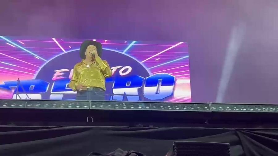 Un cantante de camisa dorada y sombrero negro frente a la pantalla con el logo del Evento Retro