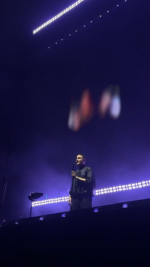 Jesús Navarro canta de negro bajo luz morada con una barra de luces detrás