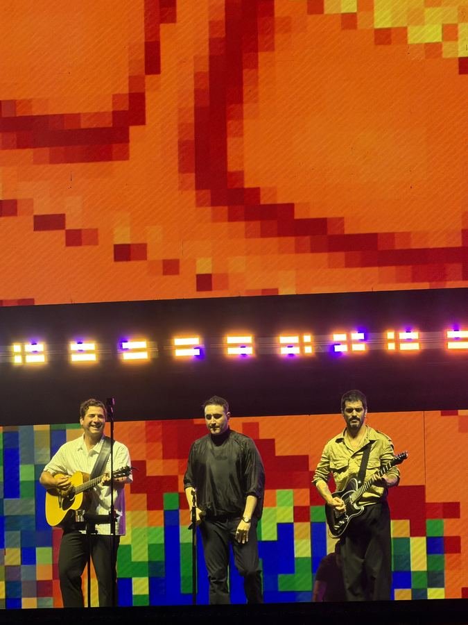 Los tres integrantes de Reik frente a la pantalla de pixeles