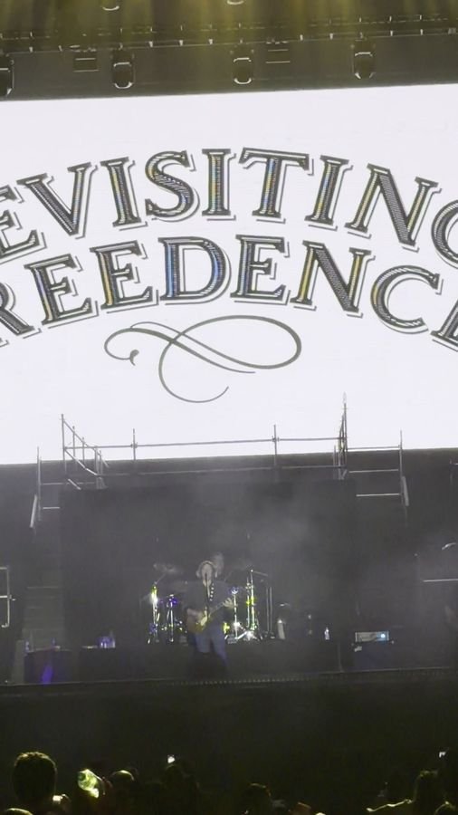 La pantalla gigante con el logo de Revisiting Creedence ocupa casi todo el cuadro sobre la banda