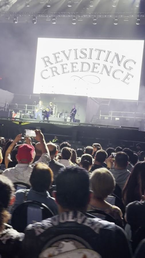 El público de pie graba con el celular frente al escenario; en primer plano, una chamarra de cuero con la palabra Revolver
