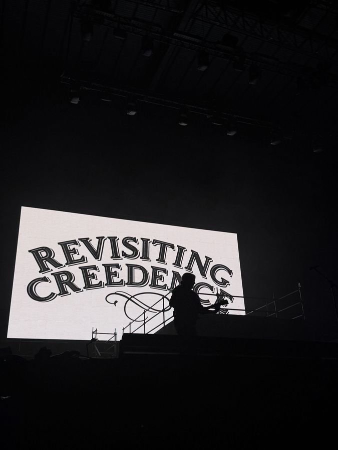 La silueta de un músico recortada contra la pantalla blanca con el logo de la banda