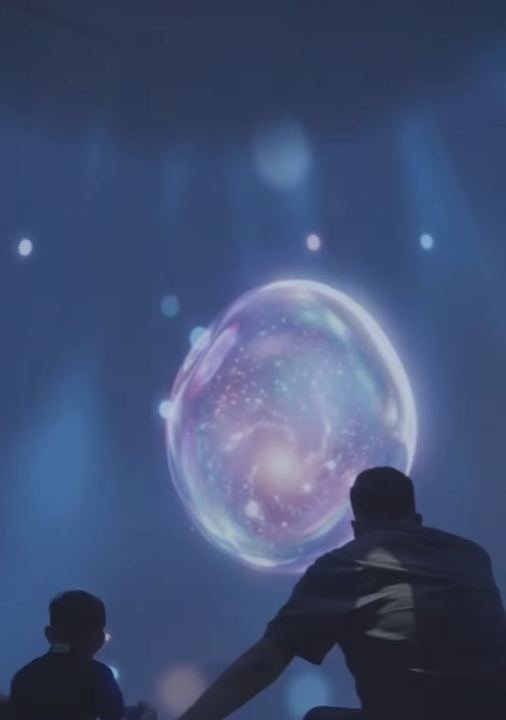 Una familia sentada en cojines mira una burbuja gigante proyectada dentro de la Domósfera
