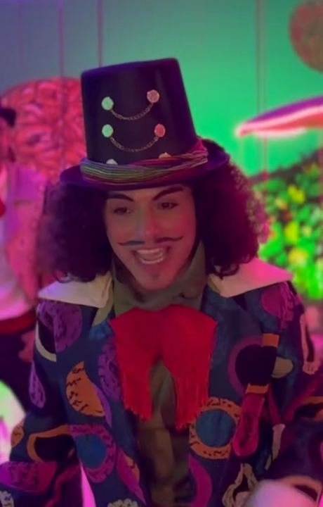 Personaje con sombrero de copa y saco de colores sonríe entre flores
